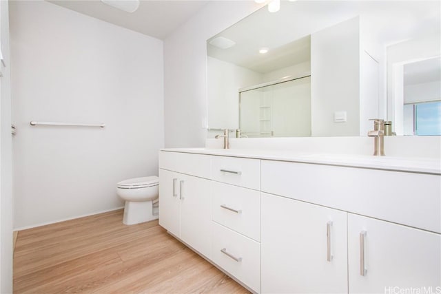 full bath featuring wood finished floors, double vanity, a sink, a shower stall, and toilet