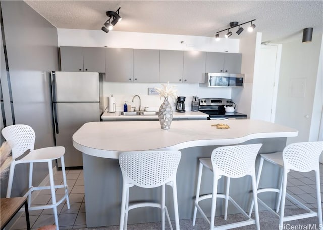 kitchen with a breakfast bar, gray cabinets, appliances with stainless steel finishes, and a textured ceiling