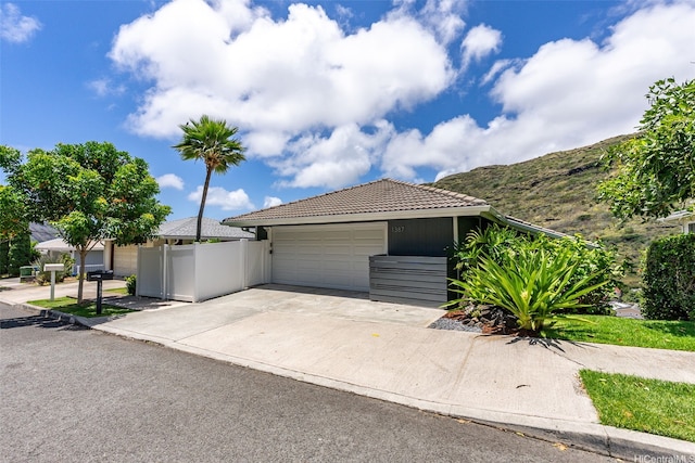 ranch-style house with fence, an attached garage, driveway, and a tile roof