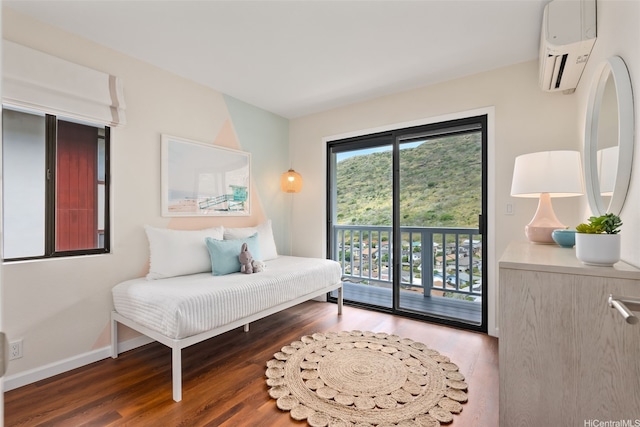 bedroom with wood finished floors, baseboards, a wall mounted AC, and access to exterior