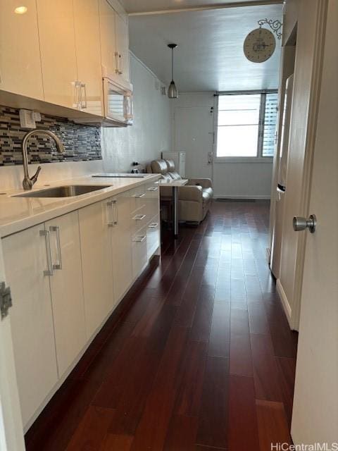 kitchen with a sink, tasteful backsplash, white cabinets, light countertops, and white microwave