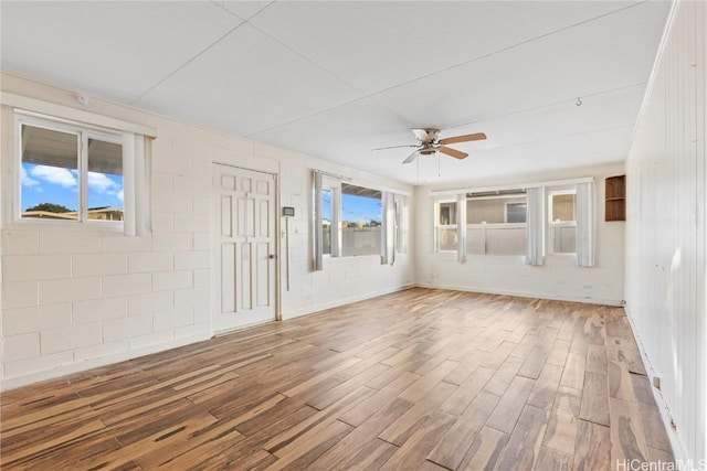 empty room with concrete block wall, wood finished floors, and ceiling fan