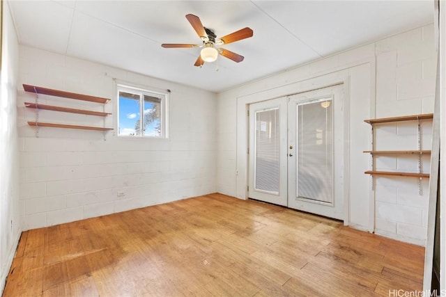 spare room featuring light wood-style flooring, french doors, concrete block wall, and a ceiling fan