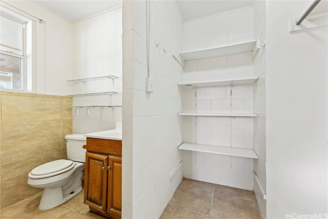 half bath with tile patterned floors, vanity, toilet, and tile walls