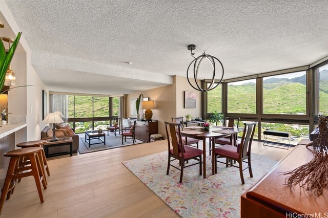 dining space featuring floor to ceiling windows, a notable chandelier, light wood-style flooring, and a textured ceiling