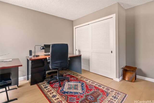 office featuring light wood-style flooring, a textured ceiling, and baseboards