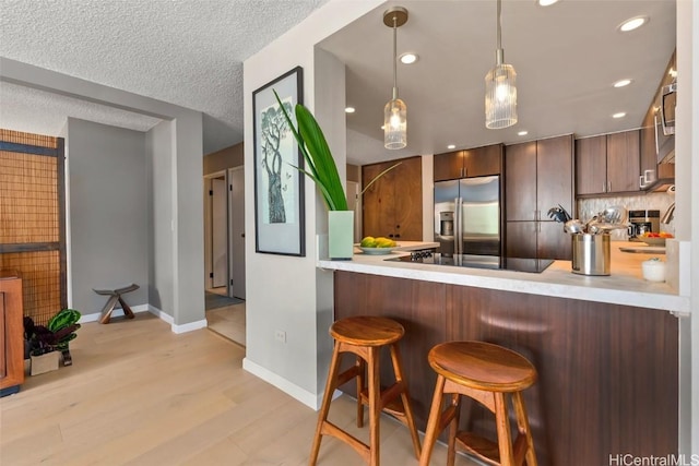 kitchen featuring light wood finished floors, black electric stovetop, stainless steel fridge with ice dispenser, light countertops, and a peninsula