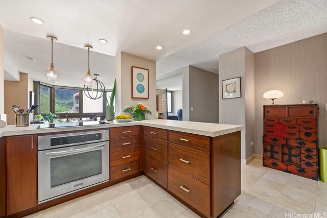 kitchen with a peninsula, oven, hanging light fixtures, light countertops, and brown cabinets