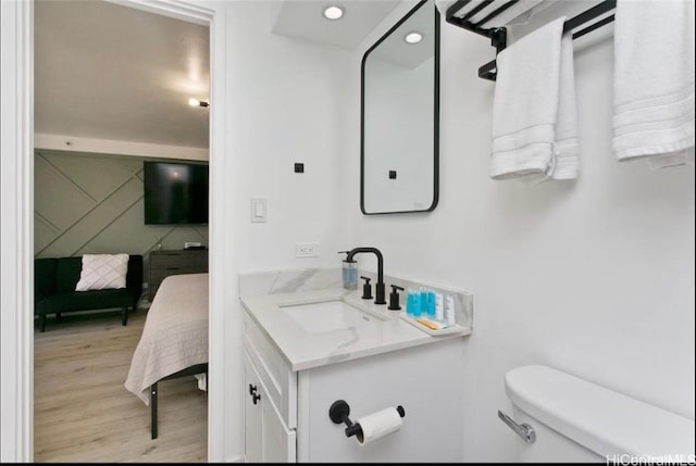 half bathroom with recessed lighting, toilet, vanity, and wood finished floors