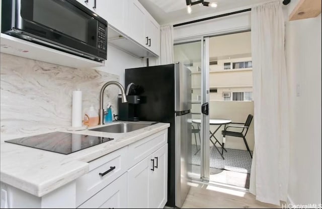 kitchen featuring backsplash, white cabinetry, black appliances, and a sink