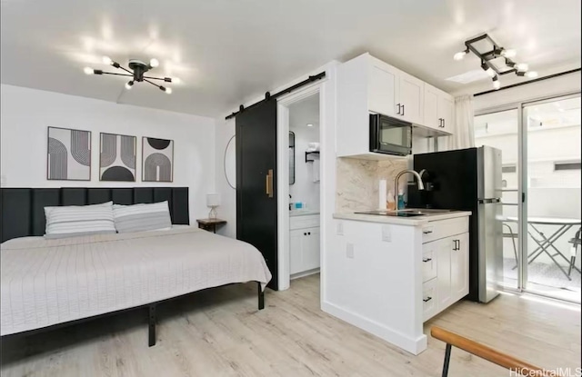 bedroom featuring connected bathroom, a barn door, light wood-style flooring, freestanding refrigerator, and a sink