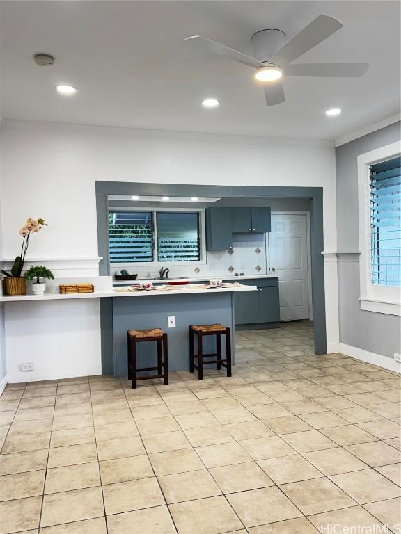 kitchen with light tile patterned floors, light countertops, a kitchen bar, and ceiling fan