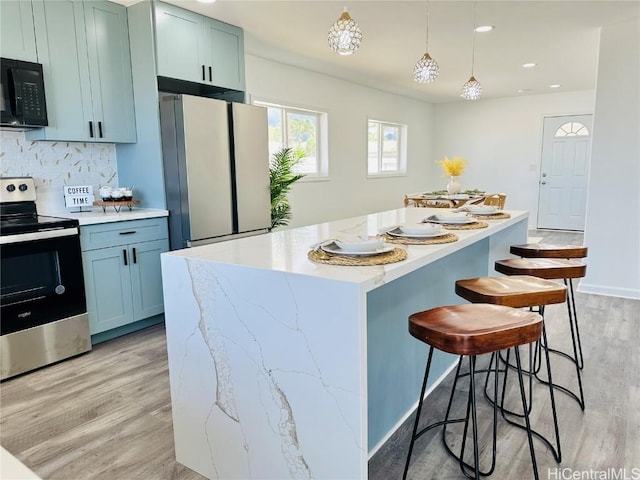 kitchen featuring freestanding refrigerator, black microwave, light wood-type flooring, a center island, and stainless steel electric range oven