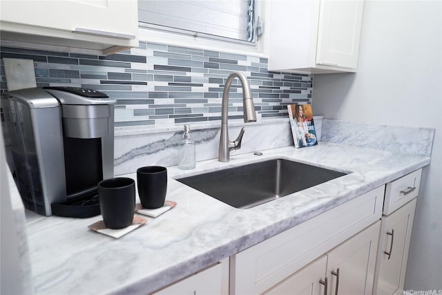 kitchen with a sink, backsplash, light stone counters, and white cabinets