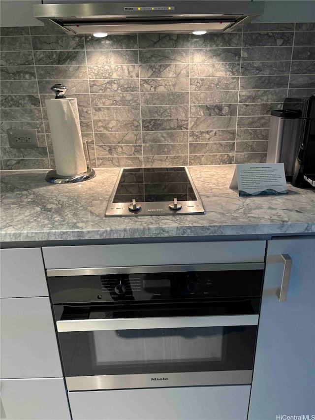 383 Kalaimoku St Unit 1106, Honolulu, HI 96815 - kitchen view of black electric cooktop, stainless steel oven, tasteful backsplash, white cabinetry, and under cabinet range hood
