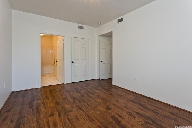 unfurnished bedroom featuring dark wood finished floors, ensuite bath, and visible vents