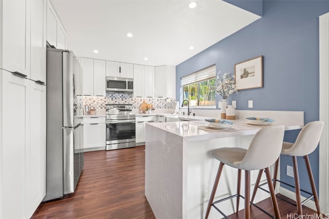 kitchen with white cabinets, a peninsula, dark wood finished floors, appliances with stainless steel finishes, and backsplash