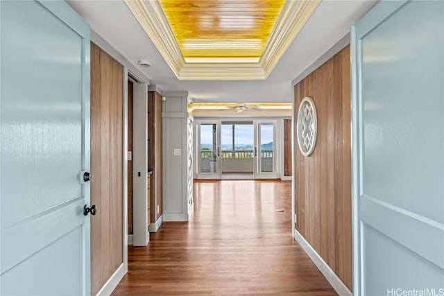 hall featuring a tray ceiling, wooden ceiling, ornamental molding, baseboards, and wood finished floors