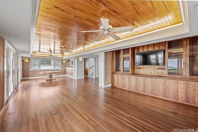 unfurnished living room with a tray ceiling, crown molding, wooden ceiling, ceiling fan, and wood finished floors