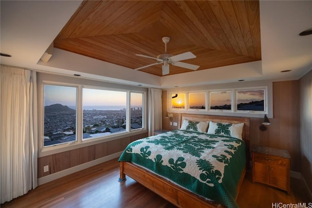 bedroom with a tray ceiling, wooden walls, wood finished floors, and wooden ceiling