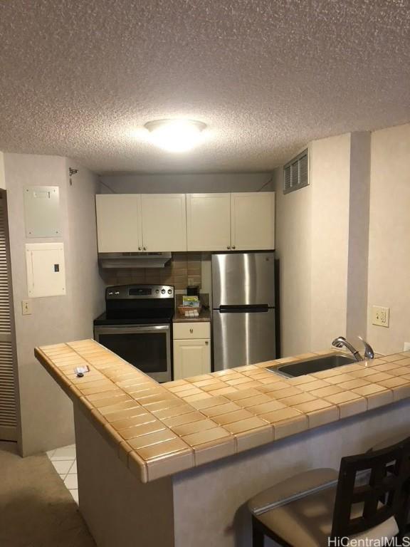 kitchen featuring visible vents, a peninsula, a sink, stainless steel appliances, and white cabinetry