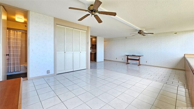 unfurnished bedroom featuring a closet, wallpapered walls, a textured ceiling, a ceiling fan, and light tile patterned floors