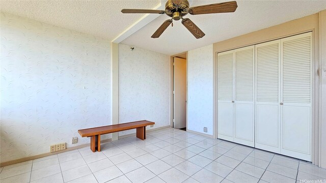 unfurnished bedroom with a closet, ceiling fan, wallpapered walls, a textured ceiling, and light tile patterned floors