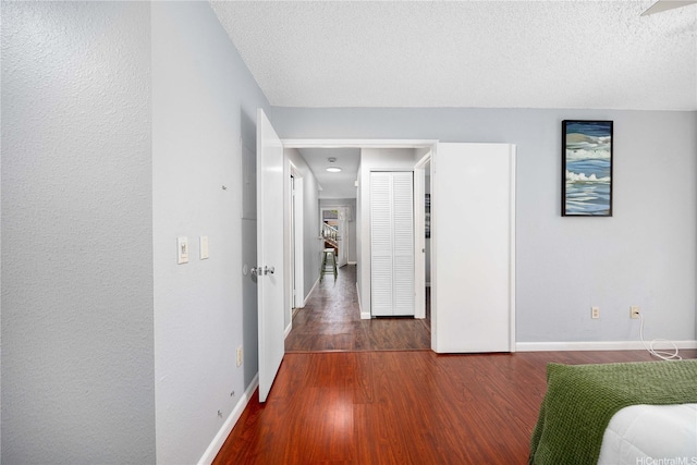 hall with baseboards, wood finished floors, and a textured ceiling