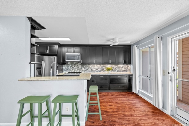 kitchen featuring stainless steel appliances, dark cabinets, a breakfast bar, decorative backsplash, and a textured ceiling