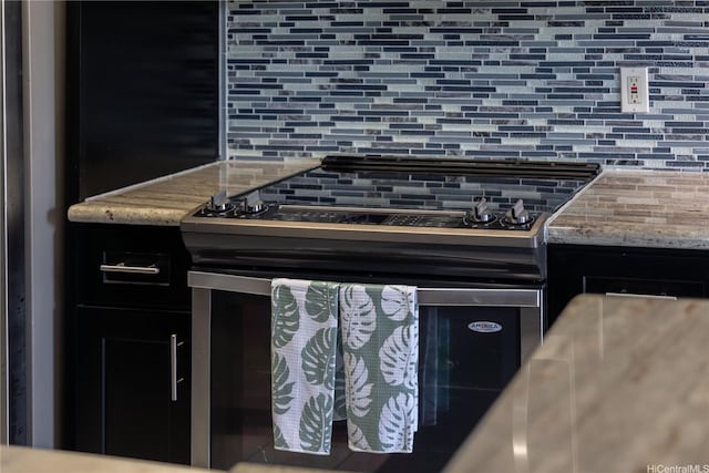 kitchen with electric range oven, backsplash, light stone countertops, and dark cabinetry