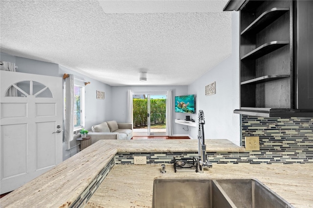 kitchen featuring a sink, decorative backsplash, open floor plan, a textured ceiling, and light stone counters
