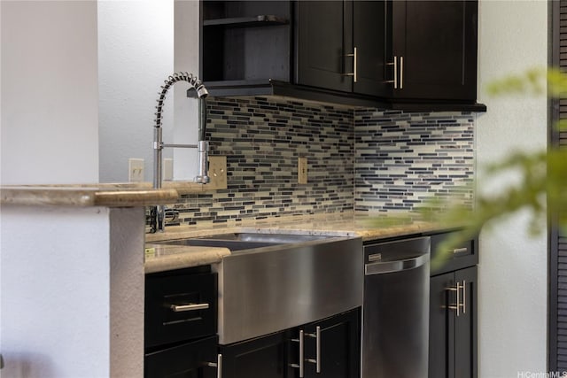 kitchen featuring a sink, stainless steel dishwasher, decorative backsplash, dark cabinets, and light stone countertops