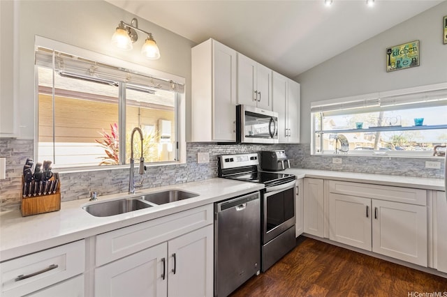 kitchen with decorative backsplash, lofted ceiling, white cabinetry, a sink, and appliances with stainless steel finishes