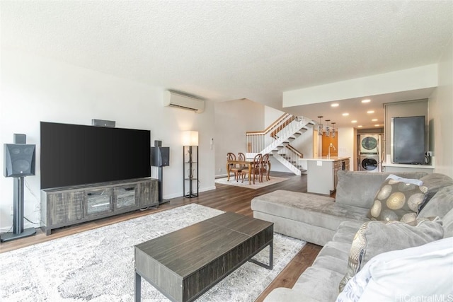 living room with a textured ceiling, stacked washer / dryer, wood finished floors, stairway, and an AC wall unit