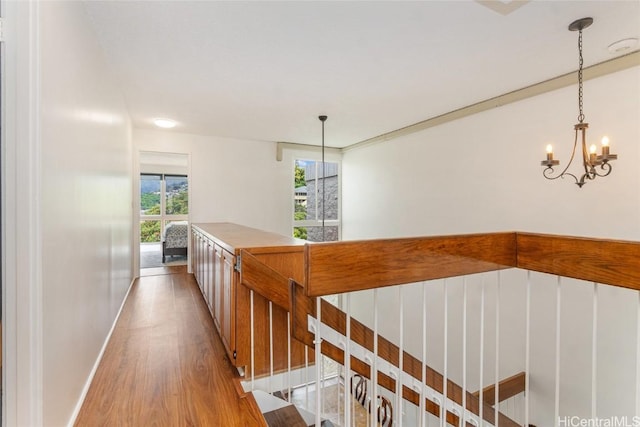 hall featuring a notable chandelier, baseboards, an upstairs landing, and wood finished floors