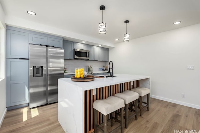 kitchen with decorative backsplash, light countertops, appliances with stainless steel finishes, a sink, and light wood-type flooring