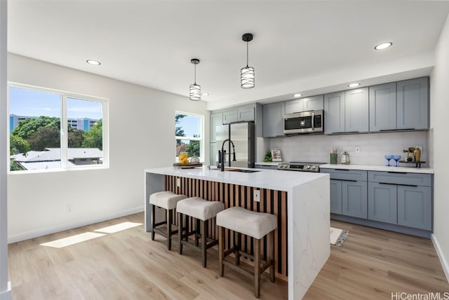kitchen featuring tasteful backsplash, stainless steel appliances, a breakfast bar, an island with sink, and light wood finished floors