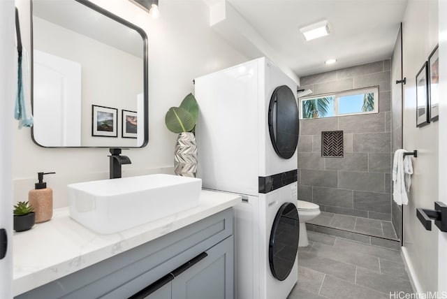 bathroom with tile patterned flooring, stacked washer and clothes dryer, vanity, a tile shower, and toilet