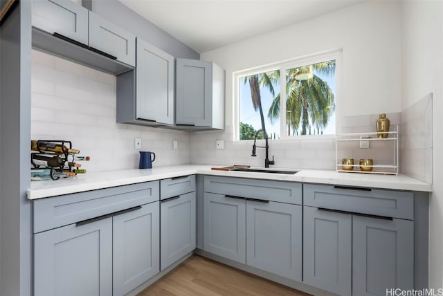 kitchen featuring light countertops, a sink, gray cabinetry, and decorative backsplash