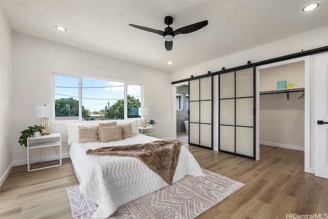 bedroom featuring a walk in closet, recessed lighting, baseboards, a barn door, and light wood finished floors