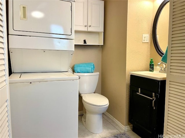 bathroom featuring baseboards, toilet, vanity, stacked washing maching and dryer, and tile patterned flooring
