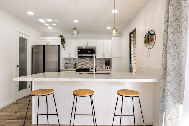 kitchen with a sink, a breakfast bar area, backsplash, white cabinets, and appliances with stainless steel finishes