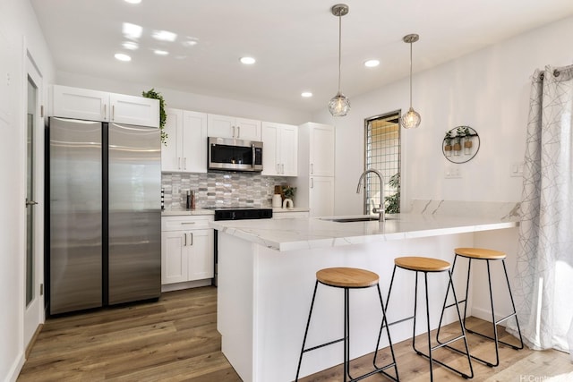 kitchen featuring white cabinets, a sink, appliances with stainless steel finishes, a kitchen bar, and a peninsula
