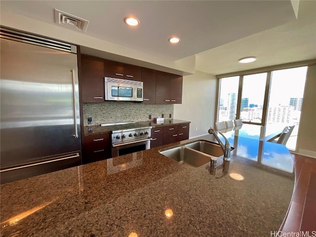 kitchen with high quality appliances, dark brown cabinetry, a sink, visible vents, and decorative backsplash