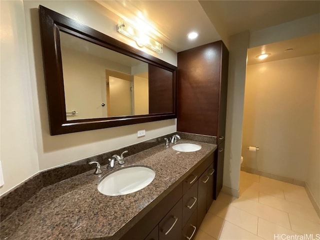 bathroom with double vanity, a sink, tile patterned floors, and baseboards