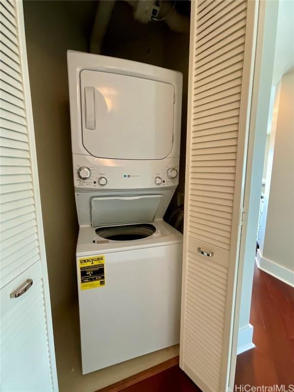 clothes washing area with dark wood-style floors, stacked washer / drying machine, laundry area, and baseboards