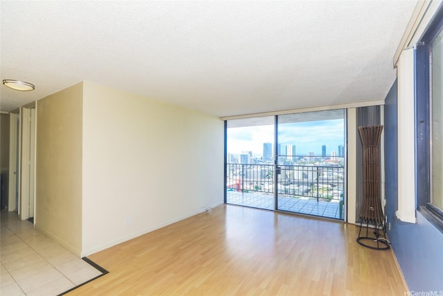 empty room featuring light wood-style flooring, a city view, floor to ceiling windows, a textured ceiling, and baseboards