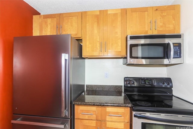 kitchen featuring stainless steel appliances, dark stone counters, brown cabinetry, and a textured ceiling