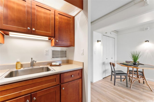kitchen featuring visible vents, brown cabinets, a sink, light countertops, and light wood-style flooring