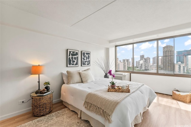 bedroom with baseboards, multiple windows, a city view, and wood finished floors
